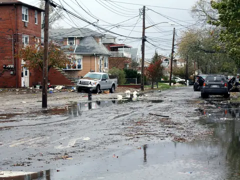 Water and storm debris across a residential street of houses in Howard Beach, Queens